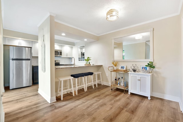 kitchen featuring stainless steel appliances, white cabinets, light wood-style flooring, and light stone countertops