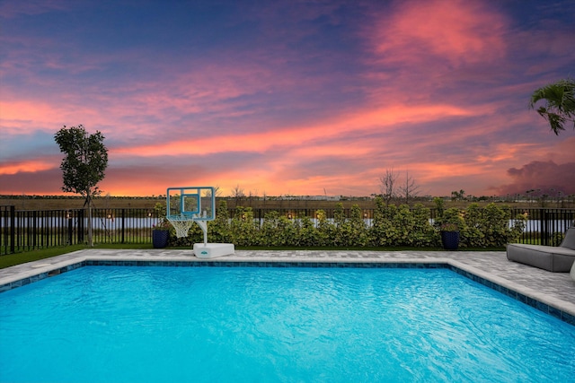 pool at dusk featuring a fenced backyard, a water view, and a fenced in pool