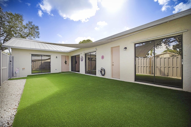 back of property with metal roof, a yard, fence, and stucco siding