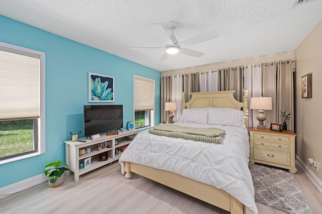 bedroom with a textured ceiling, light wood-type flooring, a ceiling fan, and baseboards