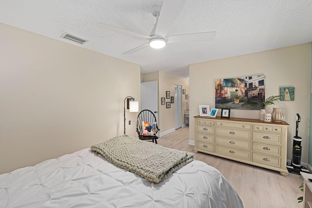 bedroom featuring baseboards, visible vents, light wood-style flooring, ceiling fan, and a textured ceiling