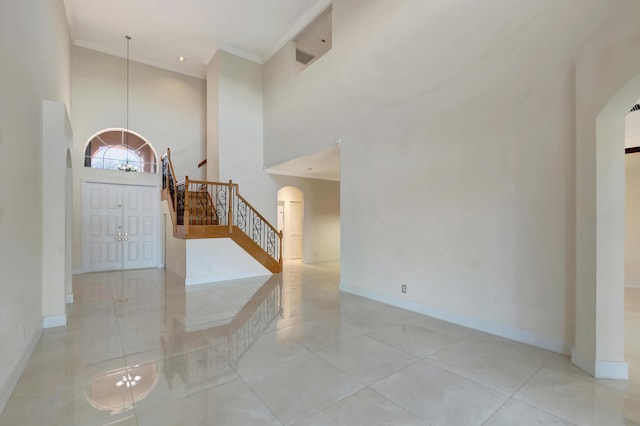 foyer entrance featuring baseboards, arched walkways, stairway, ornamental molding, and a high ceiling