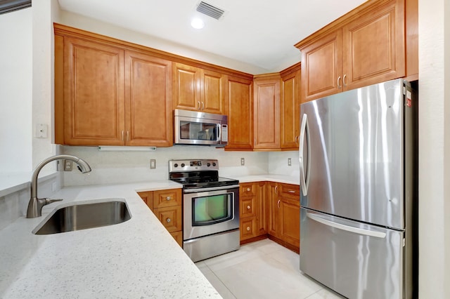 kitchen with brown cabinets, light stone countertops, stainless steel appliances, and a sink