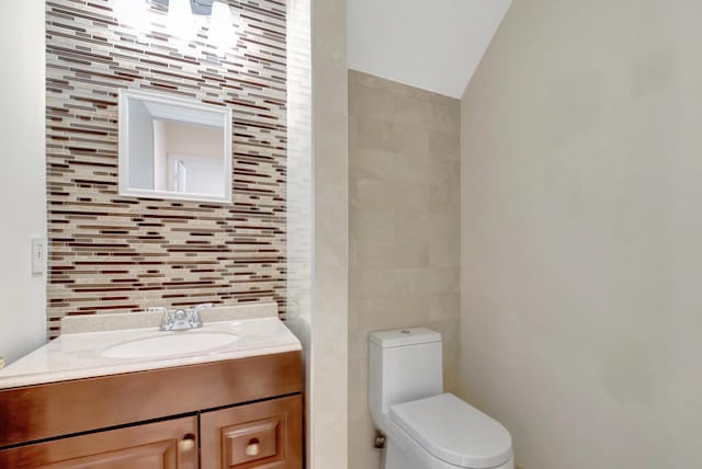 half bathroom featuring tile walls, vaulted ceiling, vanity, and toilet