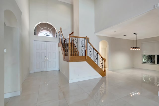 foyer with arched walkways, light tile patterned floors, a high ceiling, baseboards, and stairs