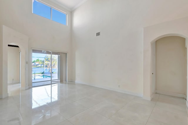 spare room with crown molding, visible vents, a towering ceiling, light tile patterned flooring, and baseboards