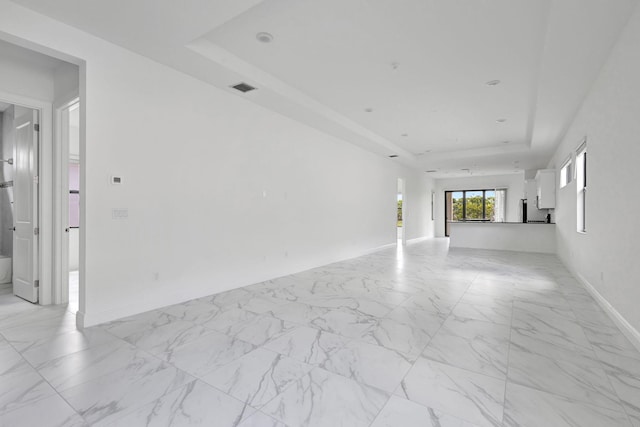 unfurnished living room featuring a raised ceiling, visible vents, marble finish floor, and baseboards