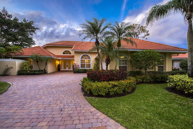 mediterranean / spanish house with a tile roof, a front lawn, decorative driveway, and stucco siding