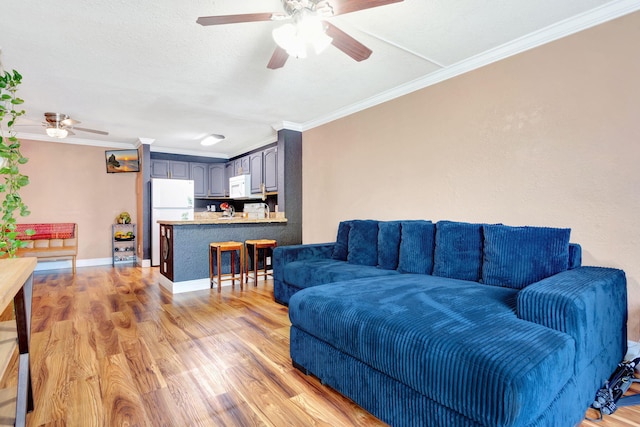 living room featuring a textured ceiling, light wood-style flooring, a ceiling fan, baseboards, and crown molding