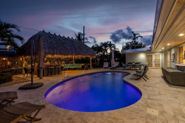 pool at dusk featuring french doors, a patio area, an outdoor pool, and exterior bar