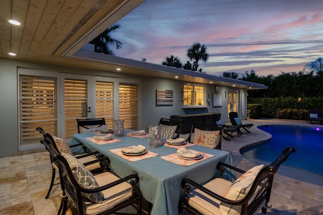 patio terrace at dusk with outdoor dining area and an outdoor pool