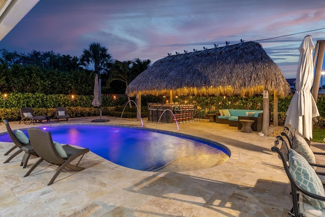 pool at dusk with a patio area, outdoor dry bar, a gazebo, and an outdoor hangout area