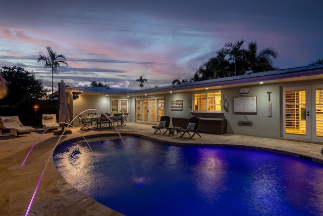pool at dusk featuring a patio, french doors, and an outdoor pool
