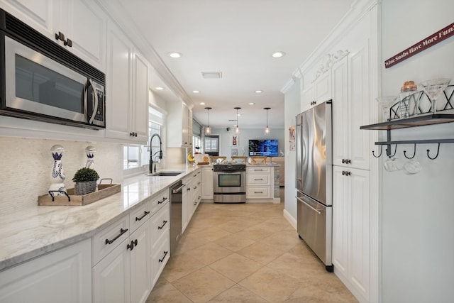 kitchen featuring a peninsula, a sink, white cabinets, appliances with stainless steel finishes, and pendant lighting