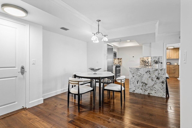 dining area with a tray ceiling, dark wood-type flooring, ornamental molding, and a notable chandelier