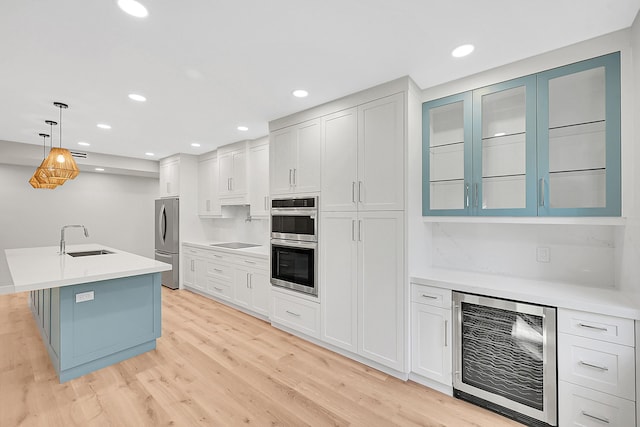 kitchen with wine cooler, light countertops, light wood-style flooring, appliances with stainless steel finishes, and a sink