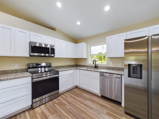 kitchen with white cabinets, lofted ceiling, light stone countertops, stainless steel appliances, and a sink