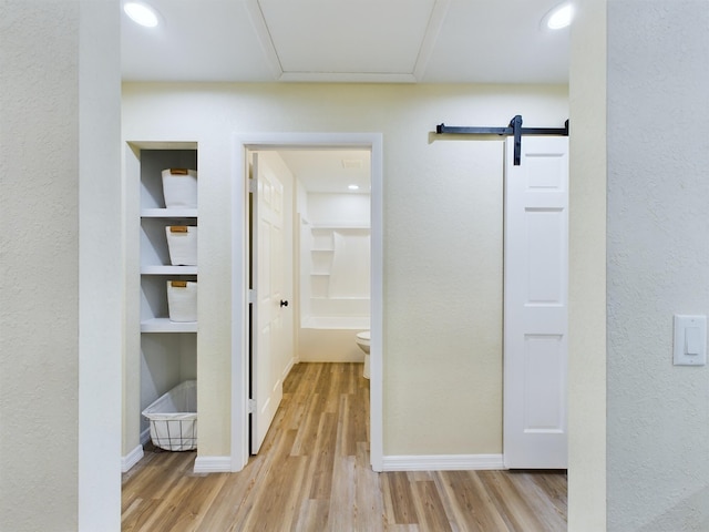 hall with built in features, light wood-style flooring, baseboards, and a barn door