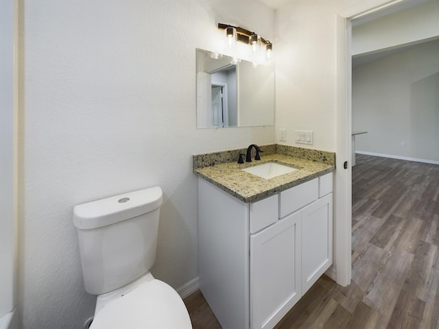 half bath with toilet, baseboards, wood finished floors, and vanity