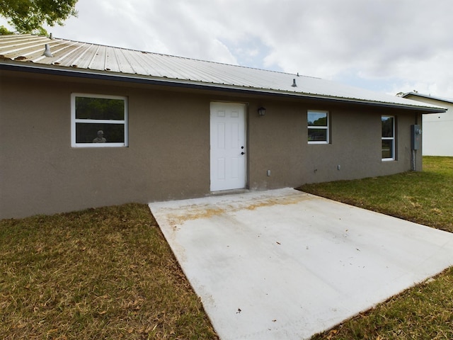 rear view of property with a patio area, a yard, metal roof, and stucco siding