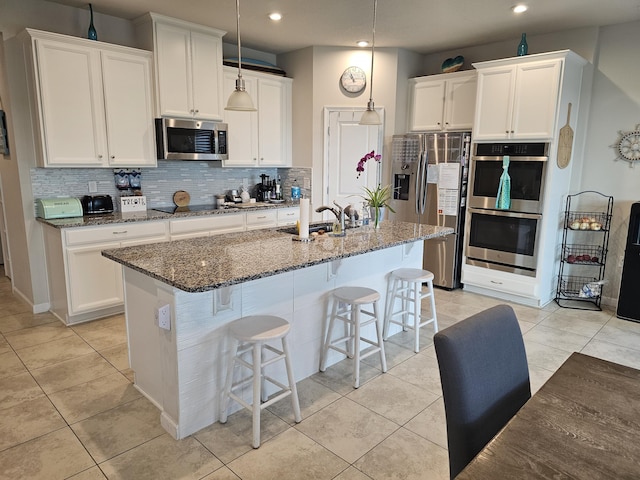 kitchen with white cabinetry, a kitchen island with sink, stainless steel appliances, sink, and dark stone countertops