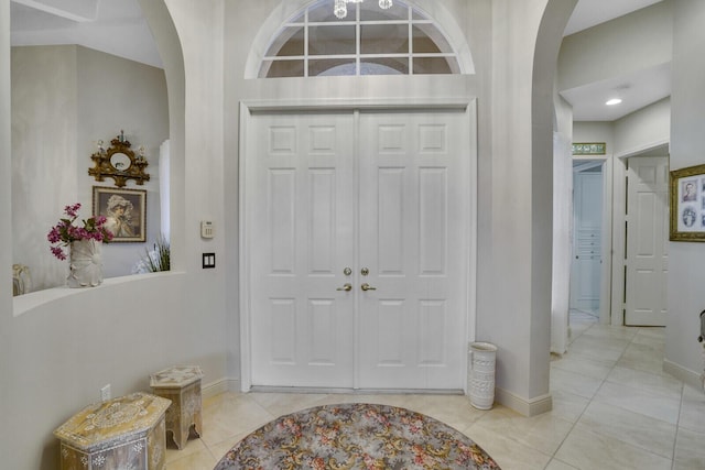 foyer with baseboards, arched walkways, and light tile patterned flooring