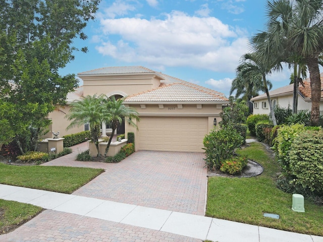 mediterranean / spanish-style home featuring a garage, stucco siding, a tile roof, decorative driveway, and a front yard