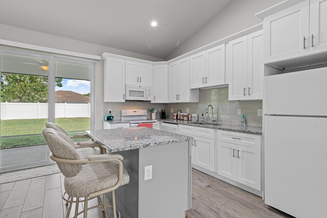 1825 SW Effland Ave, Port Saint Lucie, FL 34953 - kitchen with white appliances, a kitchen island, decorative backsplash, white cabinetry, and lofted ceiling