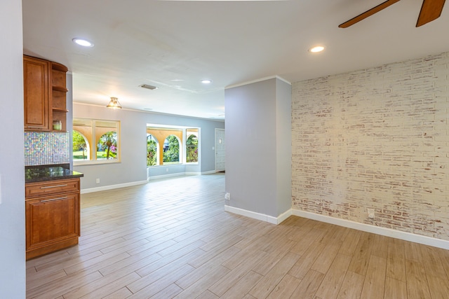 spare room featuring light wood-type flooring, baseboards, ceiling fan, and brick wall