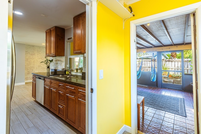 kitchen with light wood-type flooring, stainless steel appliances, backsplash, sink, and dark stone countertops