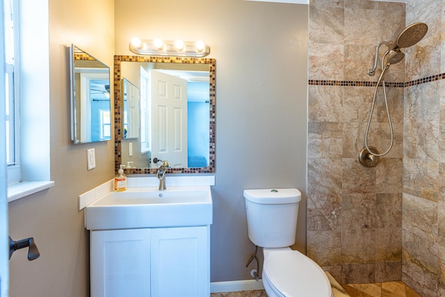 bathroom featuring toilet, a tile shower, vanity, and baseboards