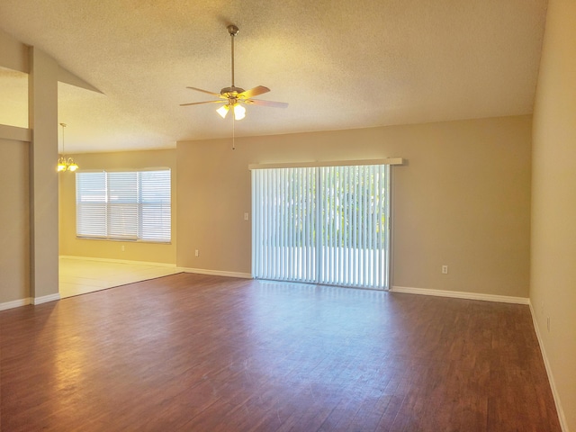 empty room featuring ceiling fan with notable chandelier, dark wood-type flooring, lofted ceiling, and a healthy amount of sunlight