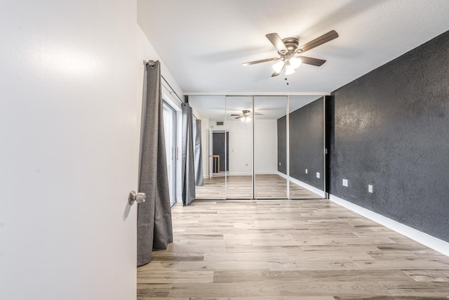 empty room with ceiling fan, a textured wall, light wood-type flooring, and baseboards