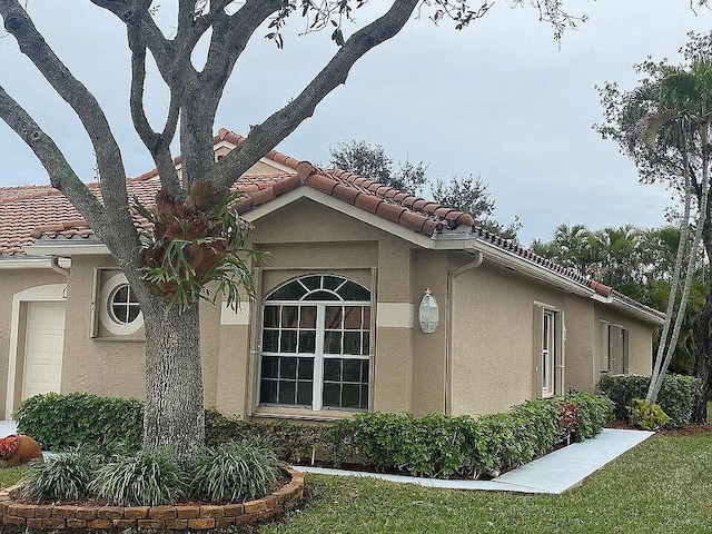 view of side of home with stucco siding, a garage, and a tile roof