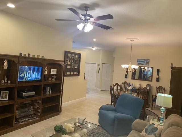 living room with ceiling fan with notable chandelier and baseboards