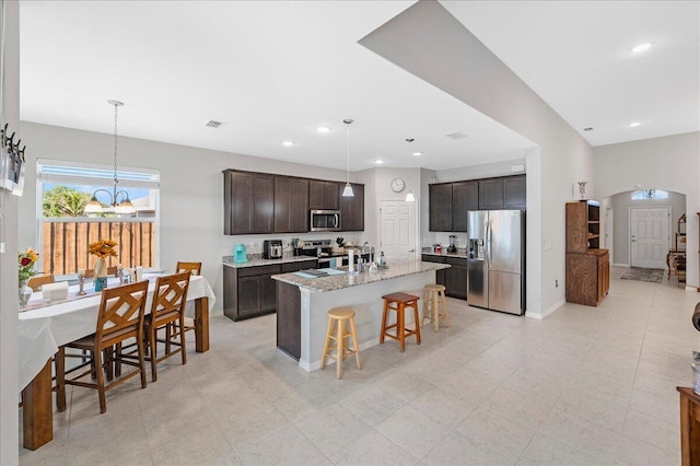 kitchen featuring a center island with sink, a kitchen bar, stainless steel appliances, hanging light fixtures, and dark brown cabinets