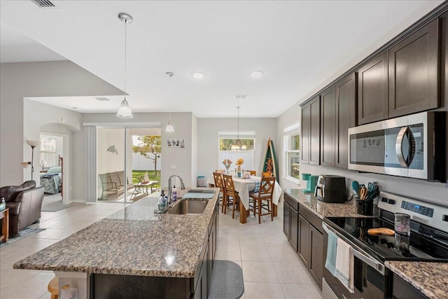 kitchen with appliances with stainless steel finishes, sink, stone counters, an island with sink, and dark brown cabinets