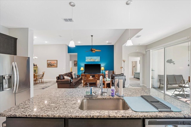 kitchen with an island with sink, decorative light fixtures, sink, light stone counters, and appliances with stainless steel finishes