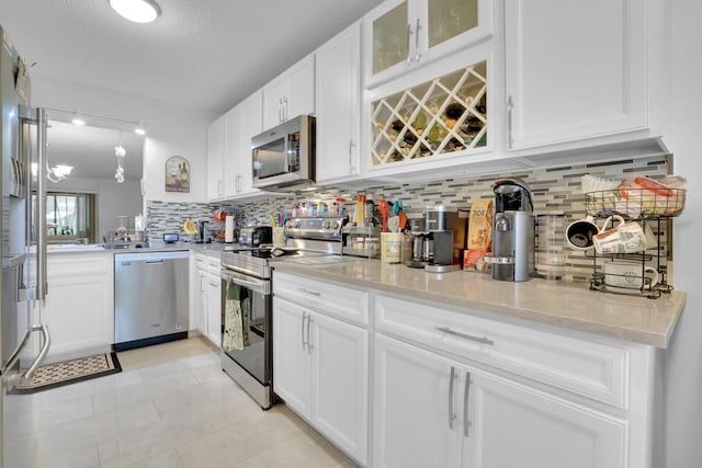 kitchen featuring appliances with stainless steel finishes, glass insert cabinets, backsplash, and white cabinetry