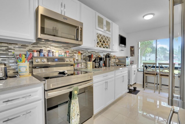 kitchen featuring light tile patterned floors, stainless steel appliances, backsplash, glass insert cabinets, and white cabinets