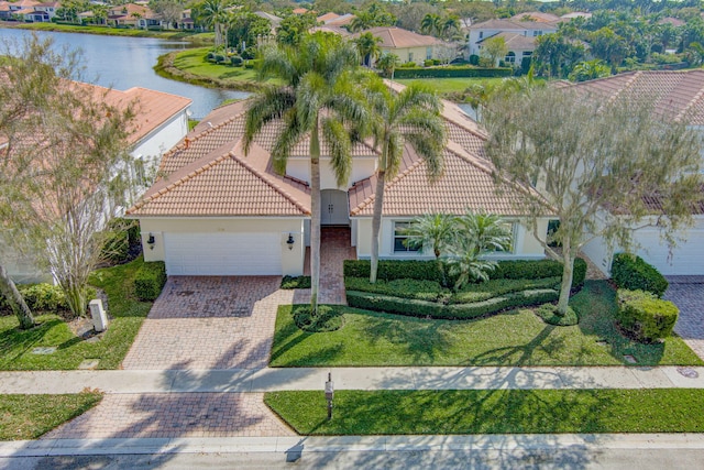 view of front of house featuring a garage, a water view, a tile roof, decorative driveway, and stucco siding