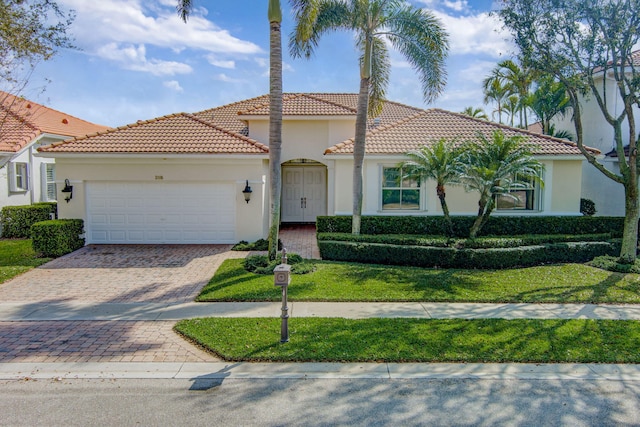 mediterranean / spanish house with an attached garage, a front yard, decorative driveway, and stucco siding