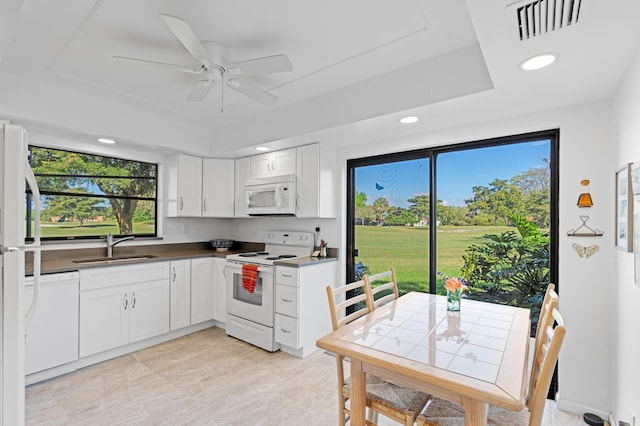 kitchen featuring white appliances, visible vents, a raised ceiling, white cabinetry, and a sink