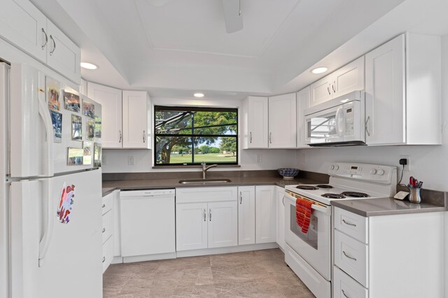 kitchen with white appliances, a raised ceiling, dark countertops, white cabinetry, and a sink