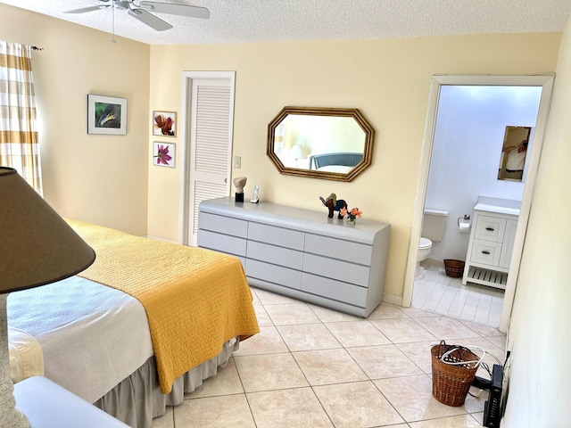 bedroom with a textured ceiling, ensuite bathroom, light tile patterned flooring, a ceiling fan, and a closet