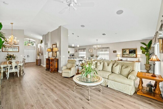 living room with light wood-type flooring, baseboards, vaulted ceiling, and ceiling fan with notable chandelier