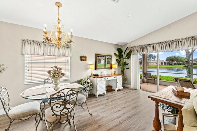dining room with lofted ceiling, light wood-type flooring, a notable chandelier, and a water view