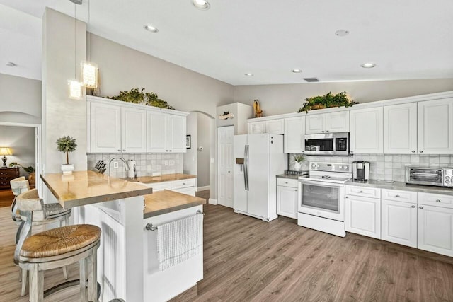 kitchen featuring tasteful backsplash, a peninsula, vaulted ceiling, white appliances, and arched walkways