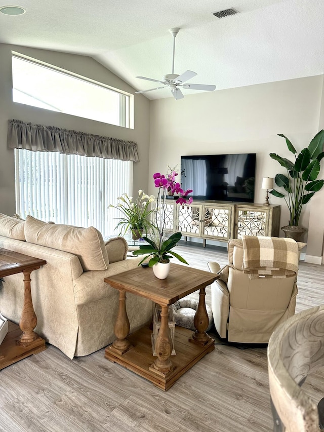 living room featuring a textured ceiling, visible vents, a ceiling fan, vaulted ceiling, and light wood finished floors