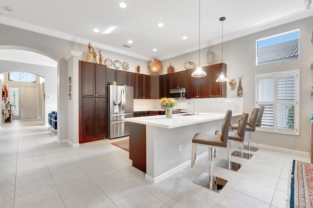 kitchen with arched walkways, light countertops, hanging light fixtures, appliances with stainless steel finishes, and a kitchen bar